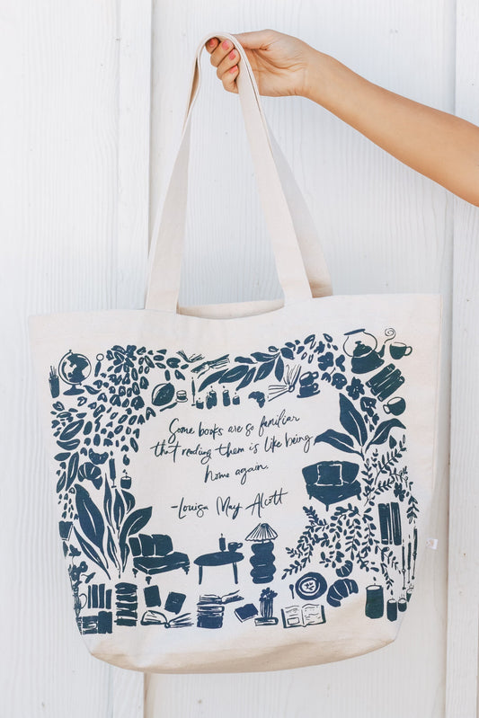 Tote bag with book-themed design and text held by a hand against a white background